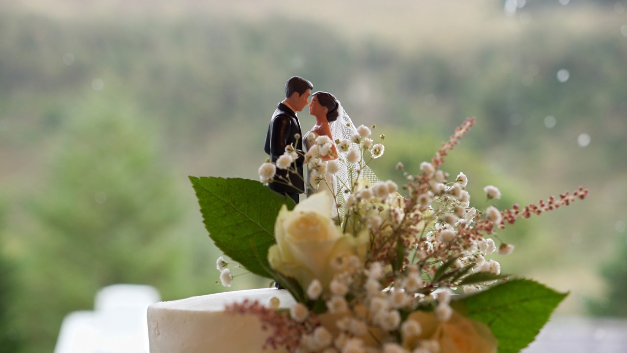 Miniature bride and groom cake topper on a floral wedding cake.