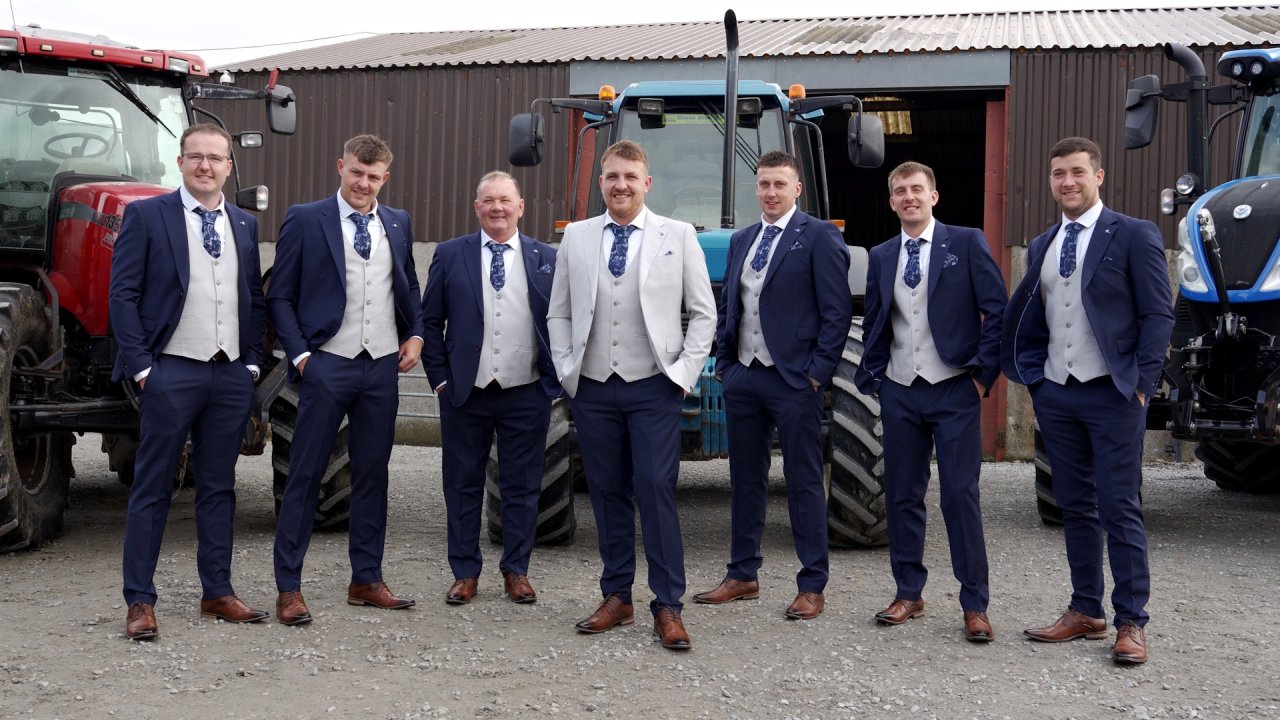 Groom Jack and his groomsmen posing in front of blue and red tractors at a farm near Donemana.