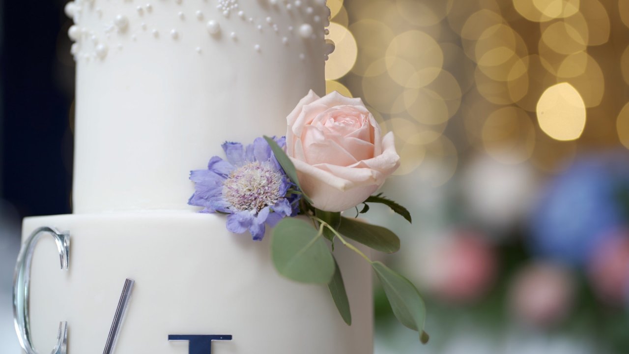 Close-up of a white tiered wedding cake decorated with a pink rose.