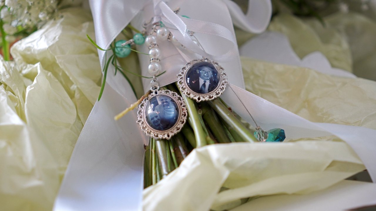 Close up of memorial photo charms attached to a white bridal bouquet with ribbon.