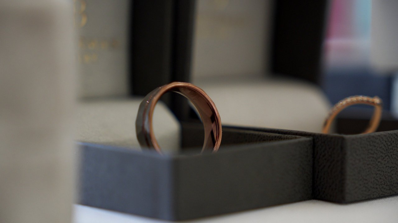 Macro shot of Jack's rose gold wedding band and Carolann's diamond-encrusted band in their display boxes.