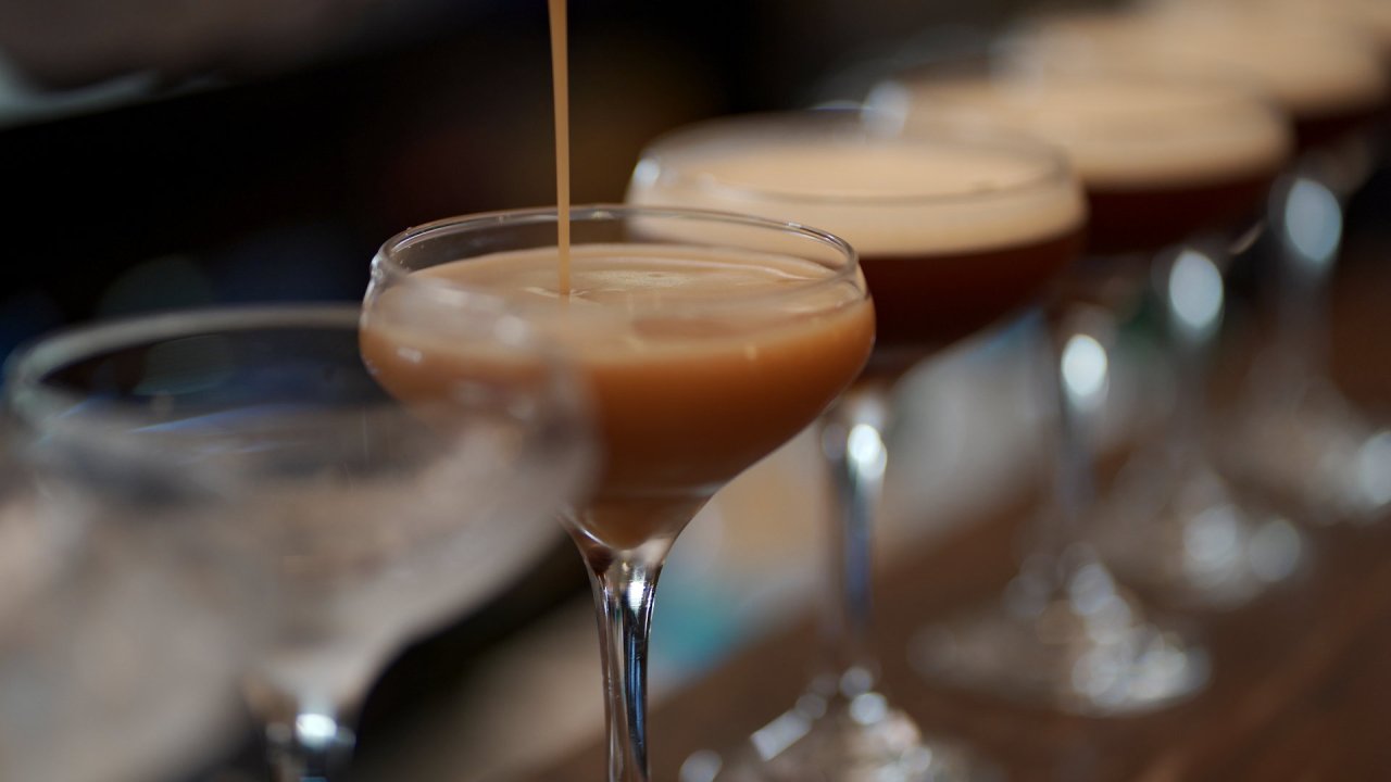 A row of espresso martinis being poured at a wedding reception bar.