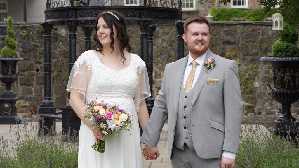 Bride Grace and Groom Christopher holding hands in front of a black wrought iron gazebo at Dunadry Hotel, Antrim.