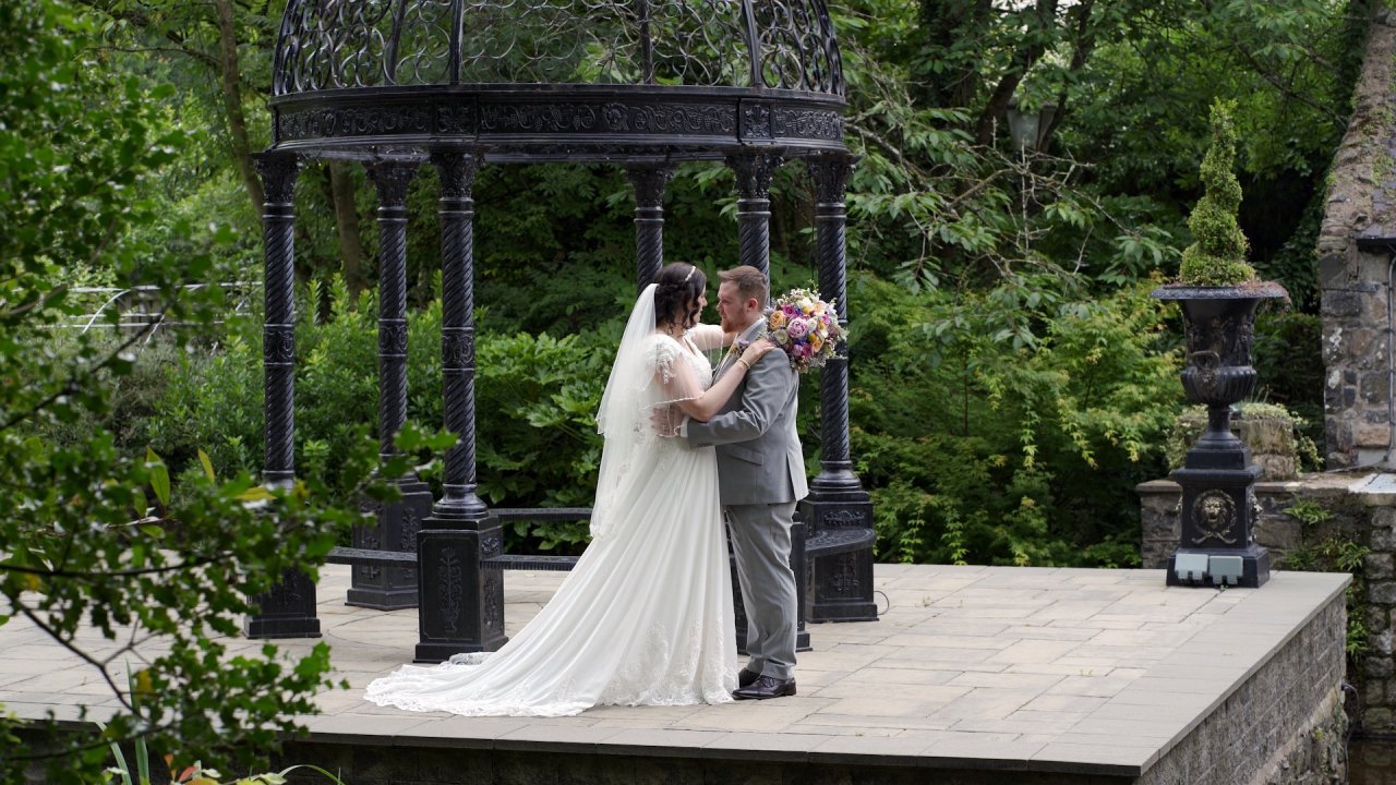 Wedding couple Grace and Christopher embracing under a decorative garden gazebo at Dunadry Hotel.