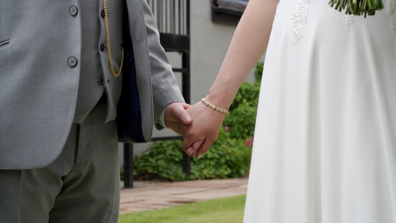 Close-up of a bride and groom holding hands, showing the bride's gold bracelet and the groom's pocket watch chain.