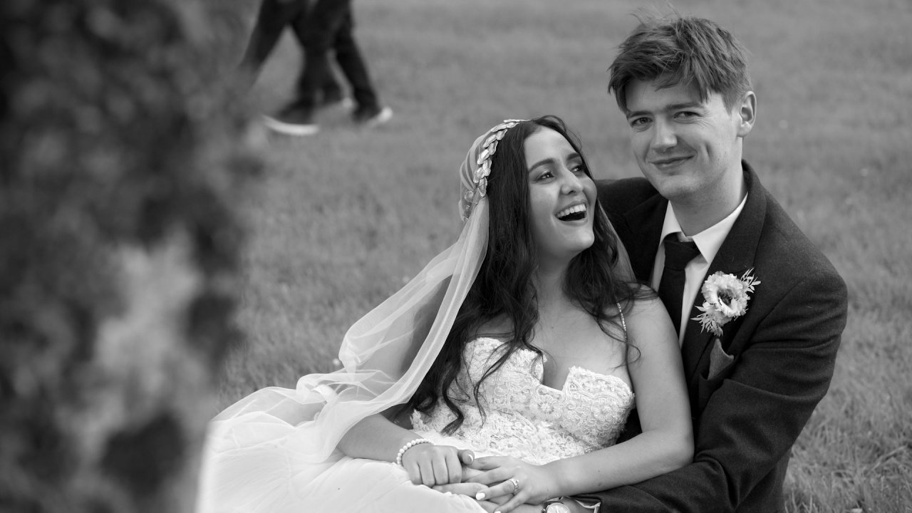 Black and white close-up portrait of a laughing bride and groom sitting on the grass.