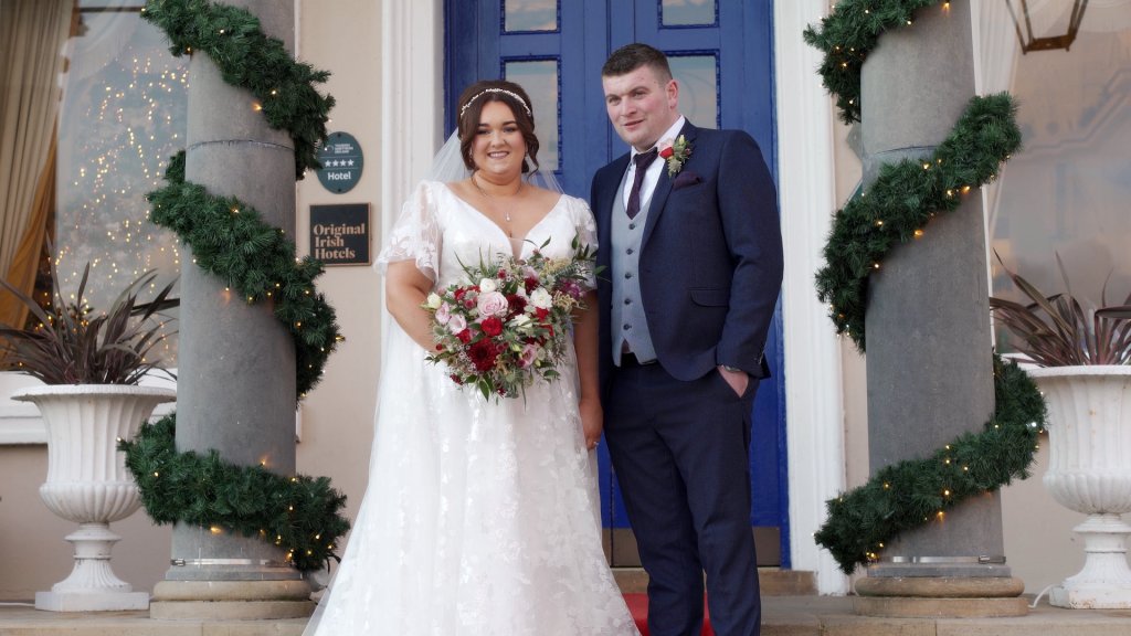 Samantha and William posing in front of the blue doors of Manor House Hotel Enniskillen with winter garland decor.