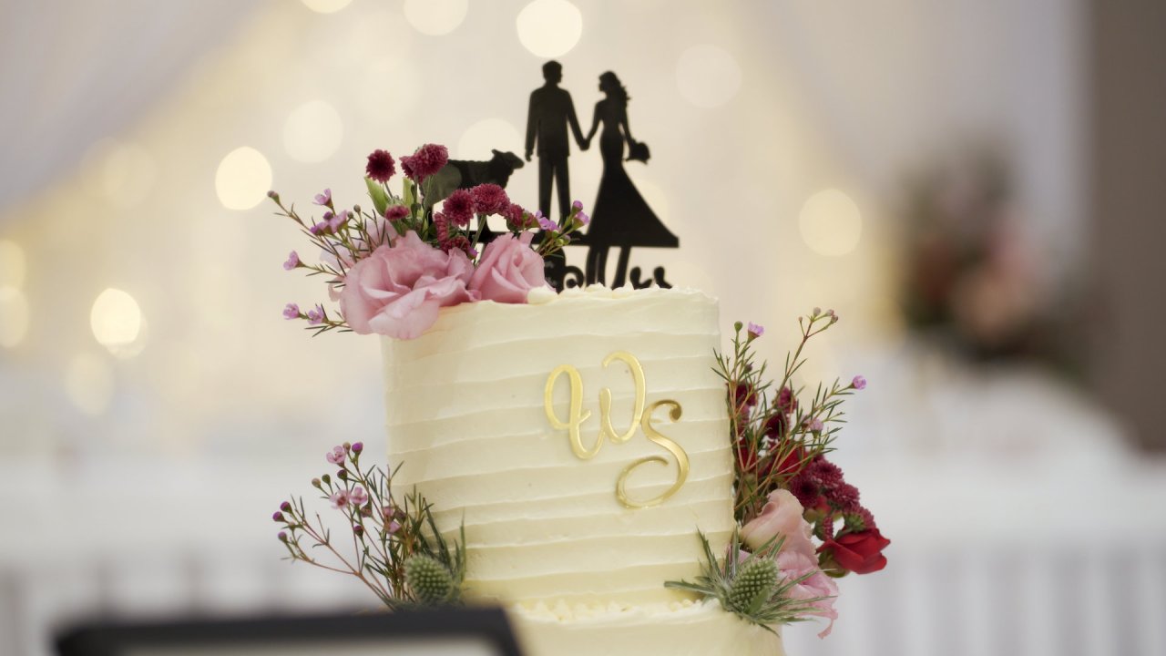 Two-tier wedding cake with gold 'WS' initials and pink floral accents.