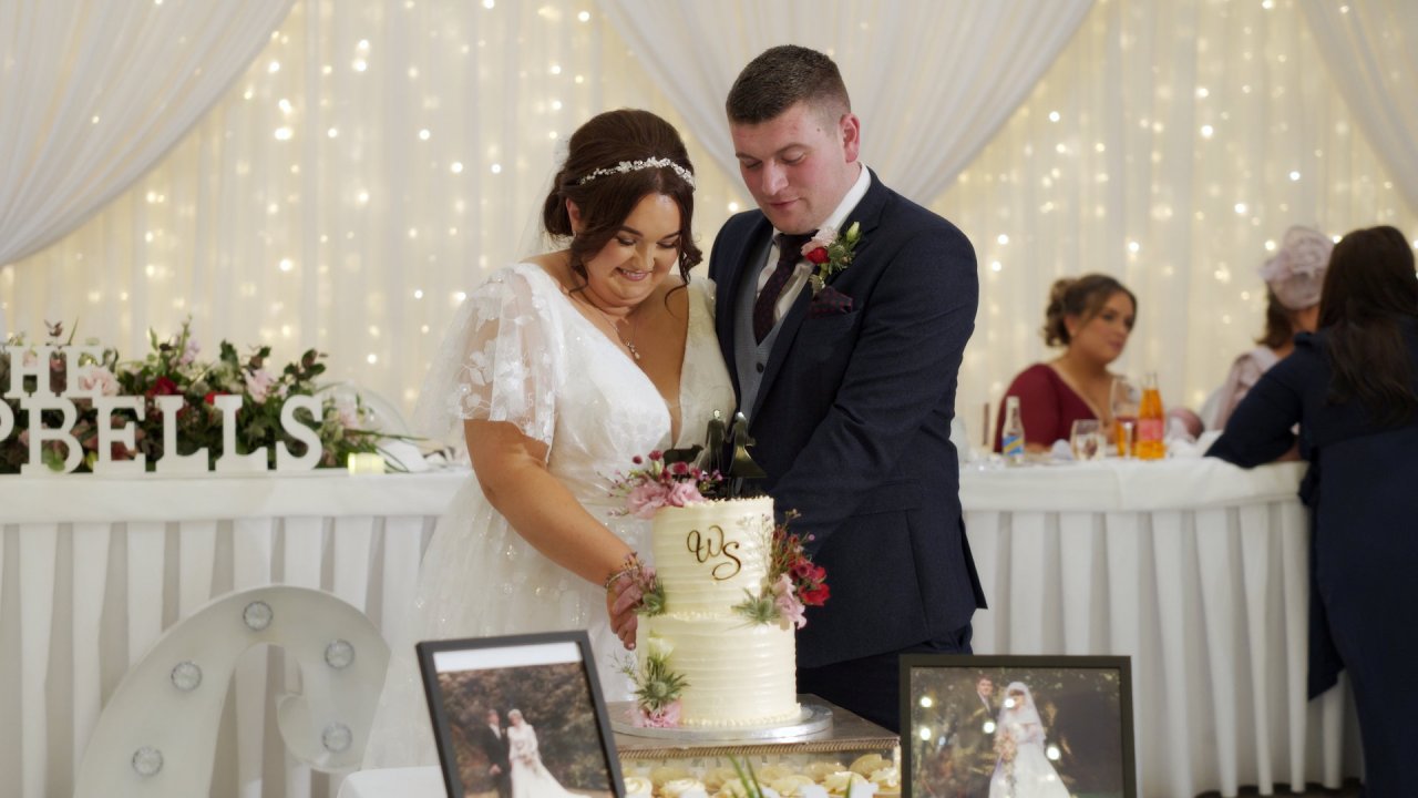 Samantha and William cutting their wedding cake in front of a fairy light backdrop at Manor House Fermanagh.