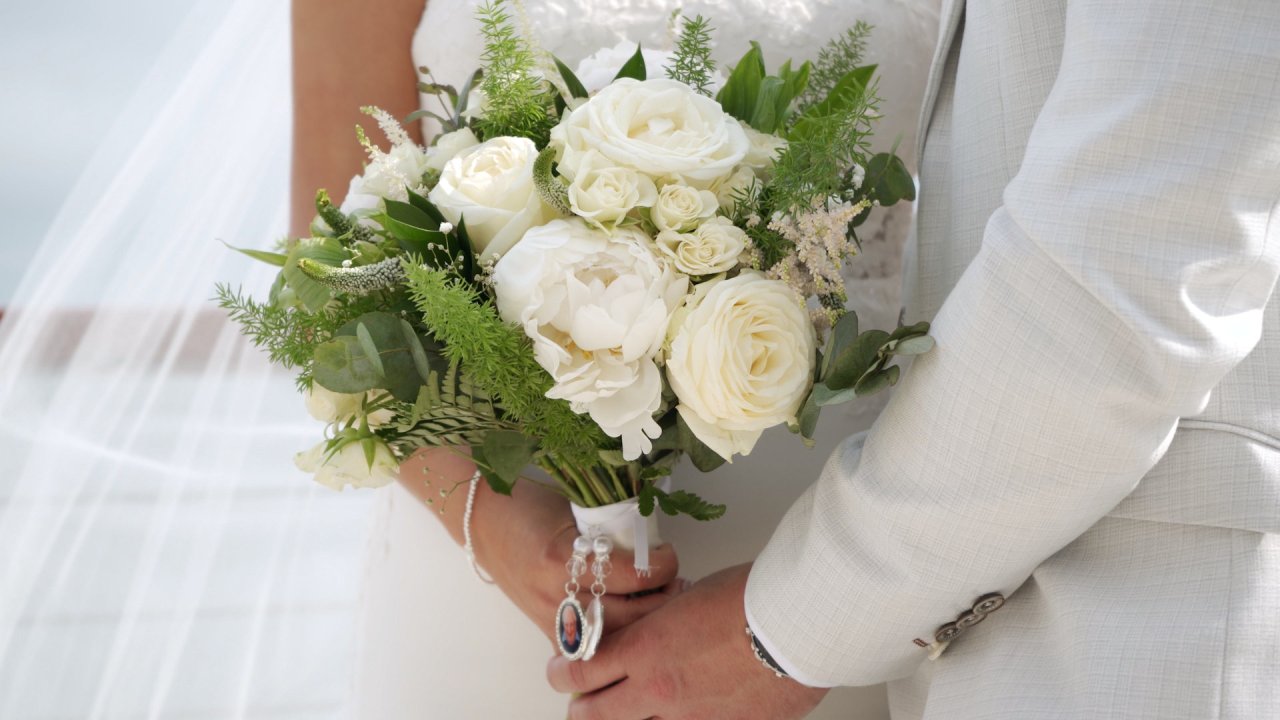 Close up of white rose and peony wedding bouquet with a memorial photo charm.