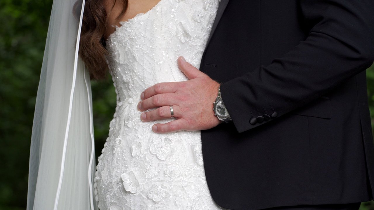 Close-up of the groom’s hand on the bride's waist, showing the wedding ring and lace dress detail.