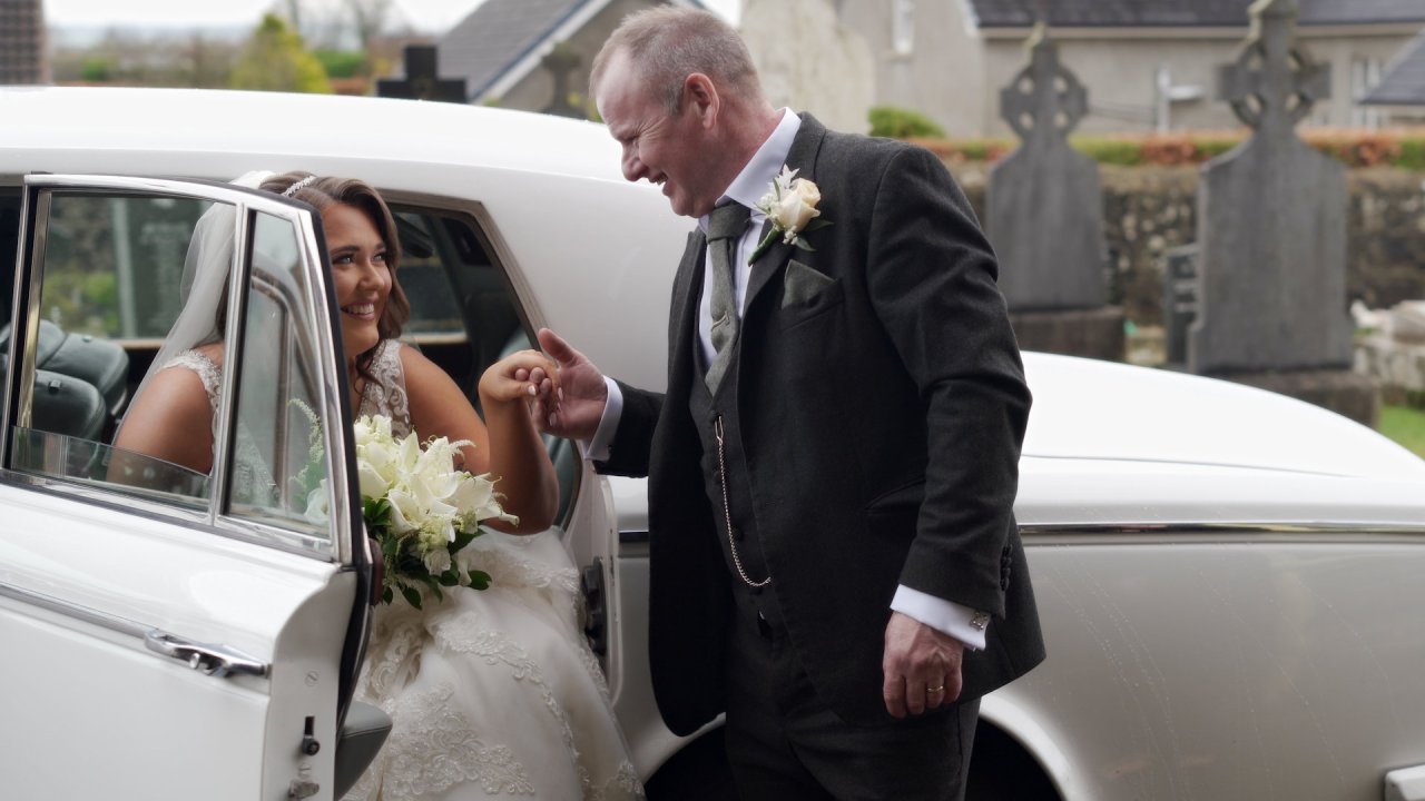 Shannon arriving at the church in a white vintage wedding car, helped out by her dad.
