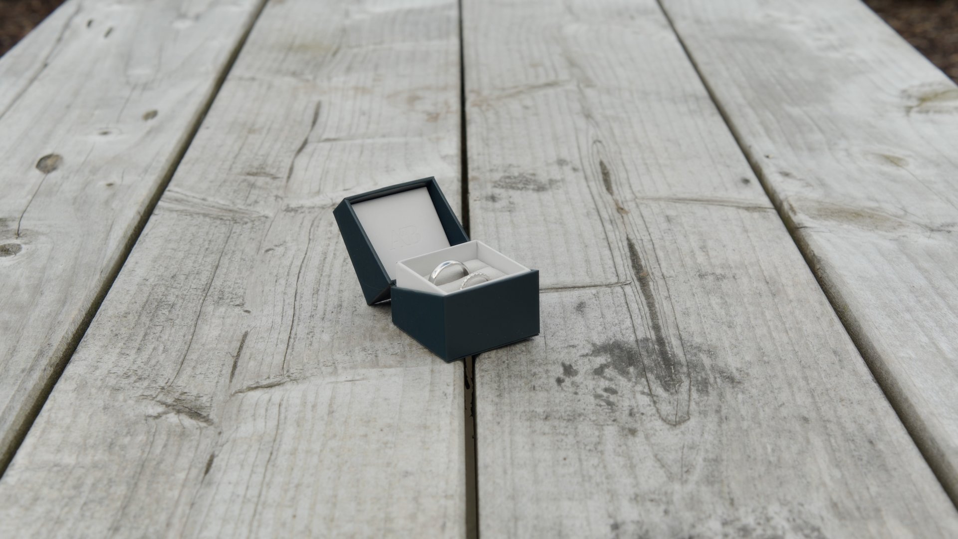 White gold wedding rings in a dark green box on a rustic wooden table at Ballyness Resort.