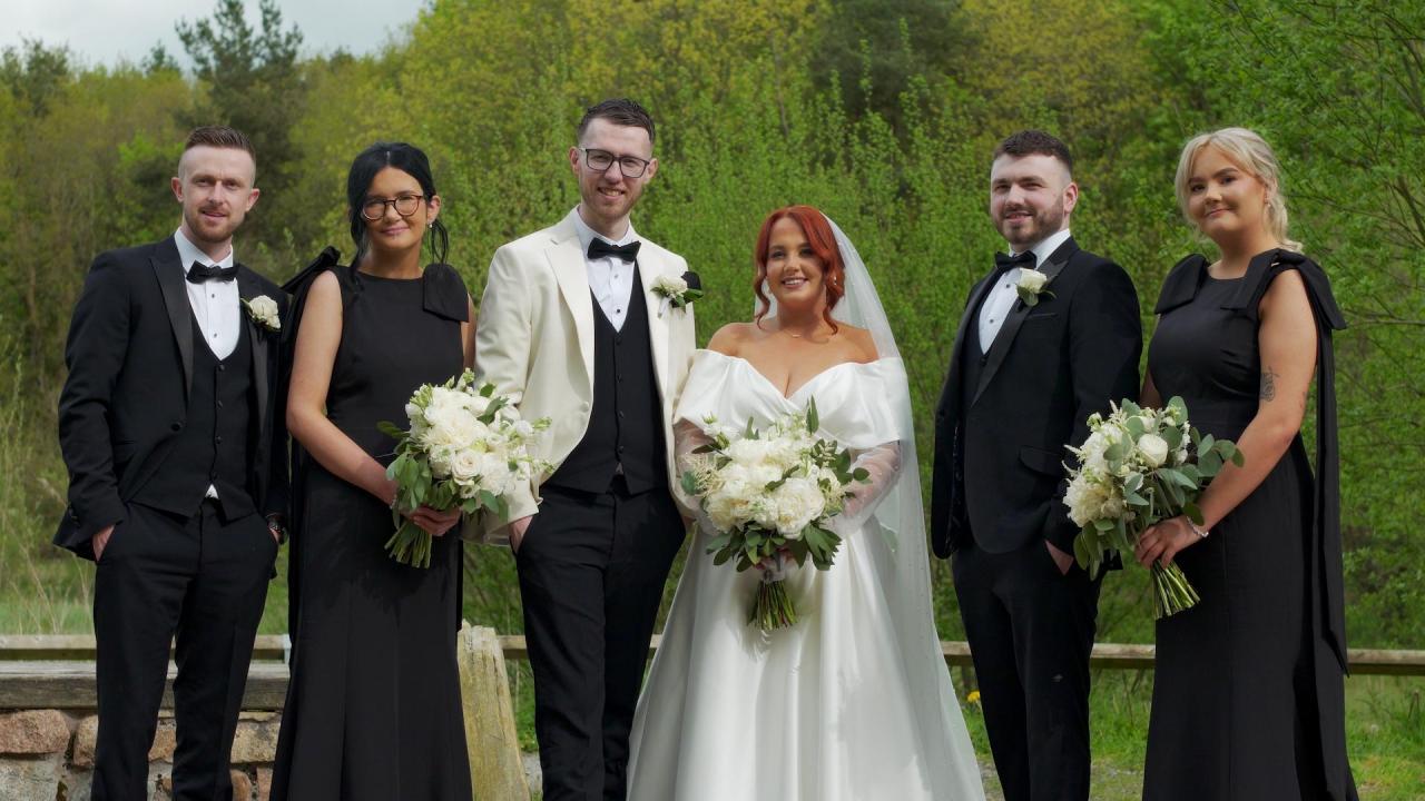 Atlanta and Sean with their bridal party at Rossmore Forest Park; bridesmaids in black dresses and groomsmen in black tuxedos.