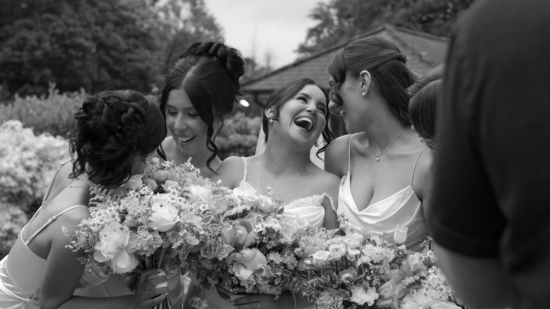 Black and white candid photo of bride Sophie laughing hysterically surrounded by her bridesmaids holding their bouquets at Beech Hill Country House.
