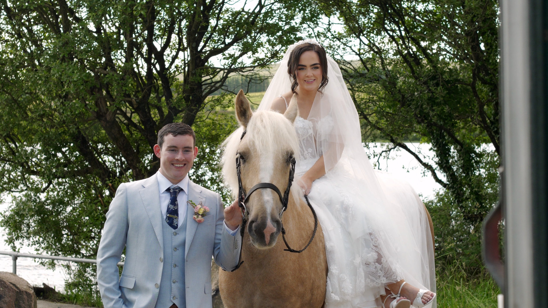 Bride Sarah smiling on horseback while groom Jason stands beside her at Moor Lough.