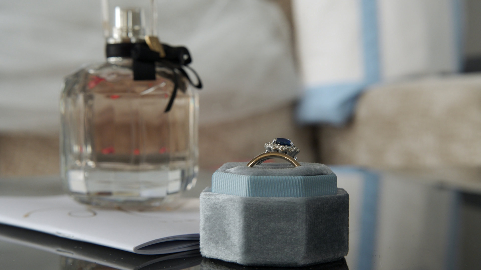 Sapphire and diamond engagement ring in a light blue velvet box beside perfume bottle during bridal prep.