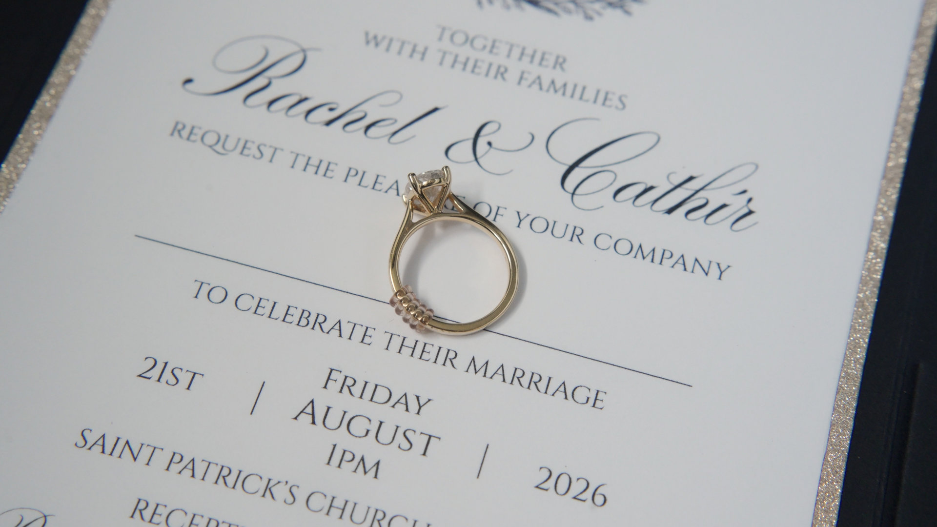 Gold engagement ring sitting on Rachel and Cathír's wedding invitation card.