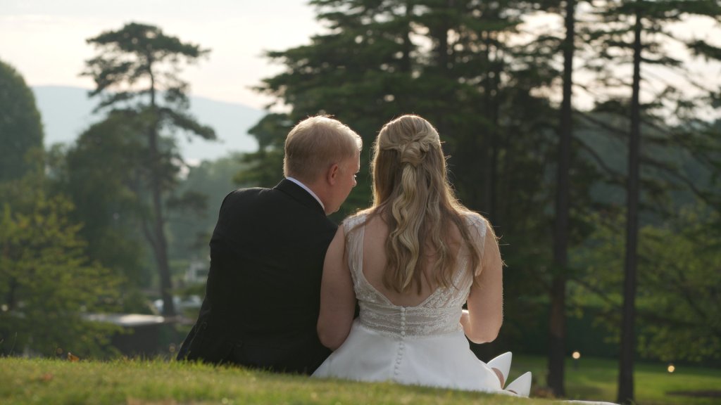 Bride and groom Leanne and Steven sitting on the lawn under dimmed eclipse sunlight at Culloden Estate.
